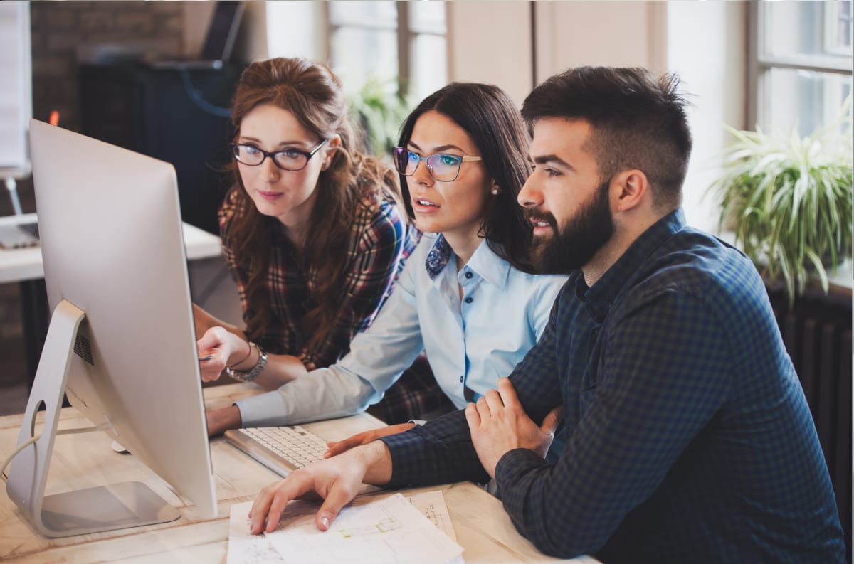Three colleagues reviewing underwriting software on a desktop monitor