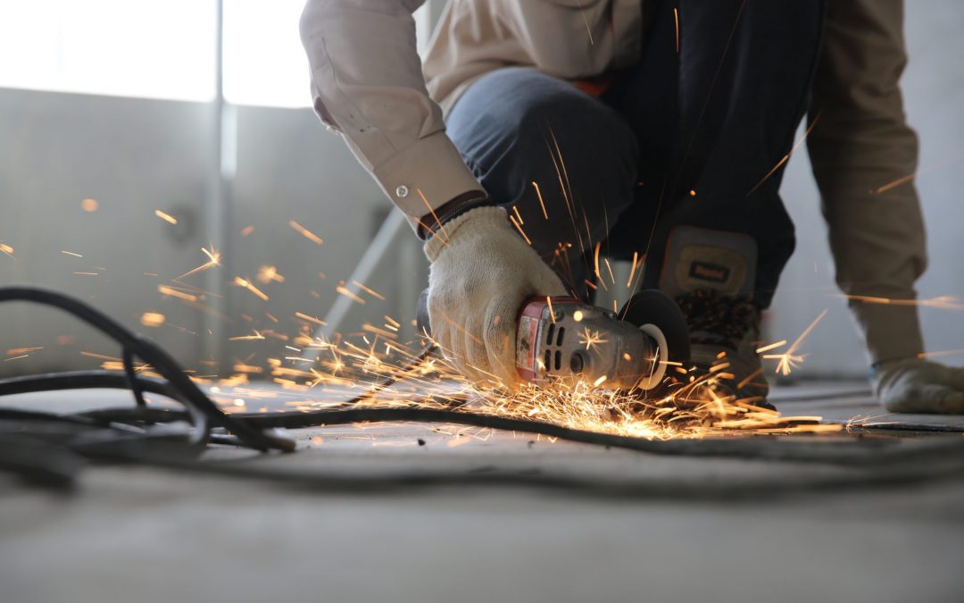 A man kneels to use a handheld metal grinder