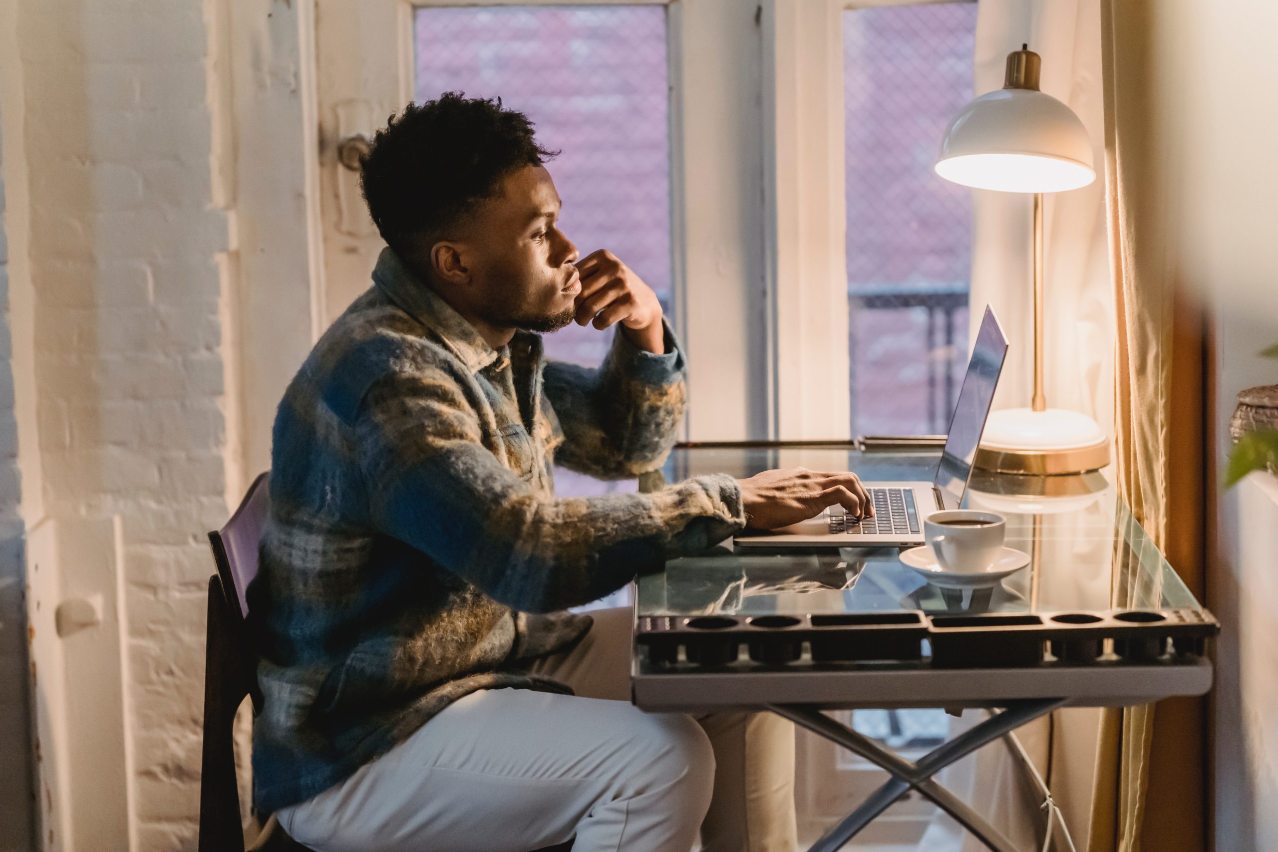 Thoughtful young man thinking at laptop with coffee cup